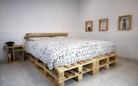 Un letto fai da te economico realizzato con pallet di legno, con un copriletto bianco e nero a tema alfabetico.