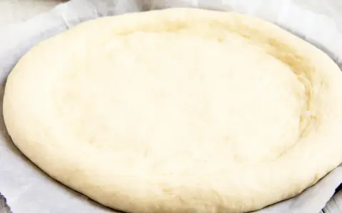 Ein runder, flacher Pizzaboden aus einem Pizzateig Rezept mit frischer Hefe, bereit für Belag und Backen.