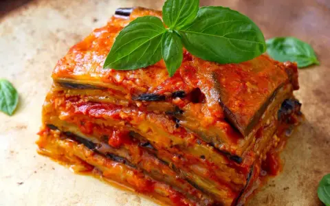 Une part généreuse d'aubergine parmigiana, empilée et nappée de sauce tomate, garnie de feuilles de basilic frais.