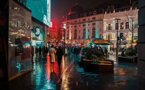 Luci al neon e riflessi sull'asfalto bagnato, la vibrante vita notturna londra pulsa tra la folla e gli edifici storici illuminati.