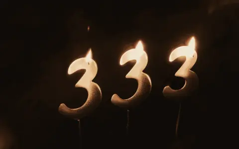 Trzy świeczki w kształcie cyfry 3, płonące w ciemności. Liczba 333 znaczenie, symbolizująca harmonię i równowagę.