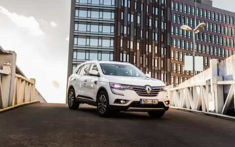 Biały Renault Koleos na tle nowoczesnego budynku. Czy warto zainwestować? Sprawdź interrisk opinie.