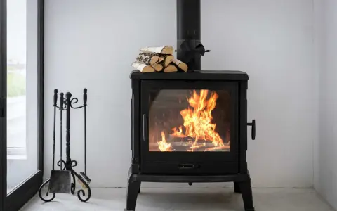 Estufa de leña con fuego vivo, lista para canalizar aire y chimenea. A su lado, un atizador y escoba.
