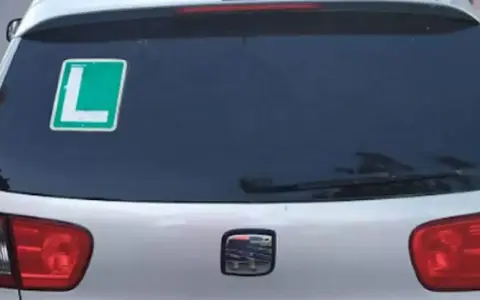 El coche tiene una L verde en la ventana trasera, indicando que el conductor está aprendiendo.