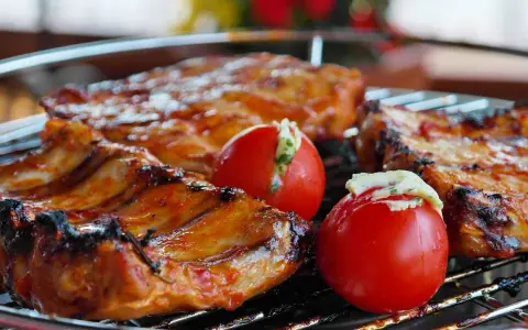 Costillas de cerdo y tomates rellenos en una parrilla. El tiempo que tarda el carbón en hacer brasa es clave para esta deliciosa cocción.