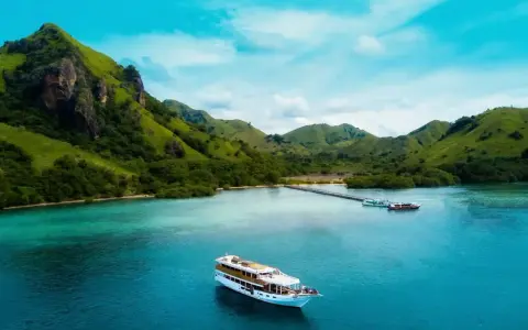 Un'isola lussureggiante con colline verdi e un mare turchese, dove si trova Bali, con una nave da crociera che naviga nelle acque cristalline.