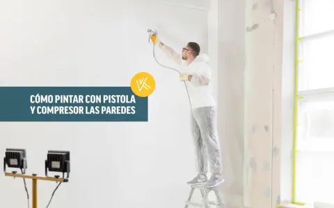 Hombre con traje protector pintando una pared con pistola y compresor.