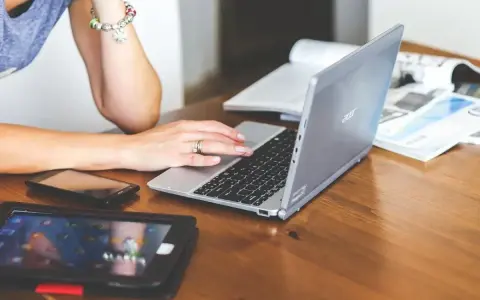 Nauczycielka pracuje na laptopie, który może być zakupiony dzięki bonowi na laptopa dla nauczycieli. Obok leżą tablet i telefon.