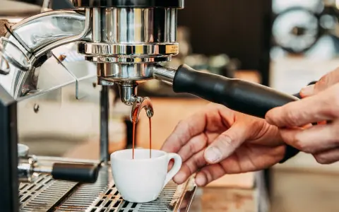 Frisch gebrühter Kaffee fließt aus der Espressomaschine in eine kleine Tasse.