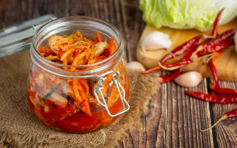 Słoik z kimchi na tle desek, z kapustą, czosnkiem i papryczkami chili.