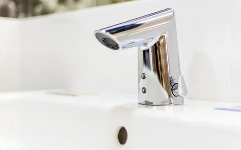 Elegancka bateria umywalkowa z korkiem, wykonana z chromowanego metalu, lśni na białej ceramice.
