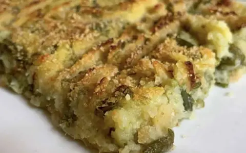 Fetta di polpettone genovese, con patate e verdure verdi, cotto al forno e cosparso di pangrattato croccante.