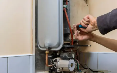 Mani che riparano uno scaldabagno a gas: il bruciatore non parte. Si vede il tecnico con un cacciavite blu.