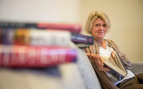 En kvinna med blont hår sitter med en bok i handen, omgiven av fler böcker. Hon ler mot kameran, som om hon delar en hemlighet från de fenomenala fruntimren på Grand Hotel.
