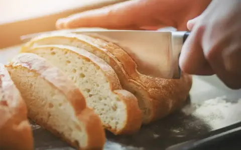 Ręce kroją świeży chleb na kromki. Dowiedz się, jak odświeżyć chleb, by był jak nowy.