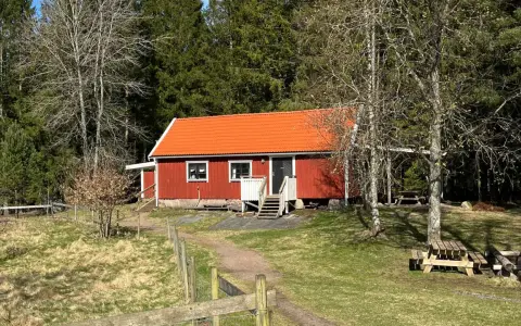 Rött torp med orange tak, omgivet av skog. En stig leder fram till torpet Freden, där picknickbord står redo för besökare.