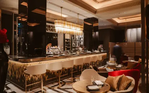 Elegante Bar mit goldenen Akzenten, weißen Barhockern und stilvollen Sitzbereichen. Ein Ort, der zu den besten Restaurants in Berlin passt.