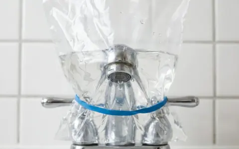 Un sac en plastique rempli d'eau est attaché à un robinet avec un élastique bleu. Une méthode pour enlever le calcaire de l'eau naturellement.