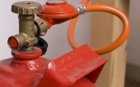 Détail d'une bouteille de propane rouge avec détendeur et tuyau orange, illustrant la norme d'installation gaz propane bouteille.