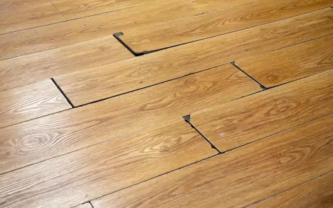 Suelo de madera con tablas levantadas y espacios oscuros, indicando posible daño por humedad. Se busca cómo quitar mancha negra humedad madera.