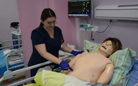 Studentka stomatologii ćwiczy procedury medyczne na fantomie. Monitor parametrów życiowych pokazuje dane.