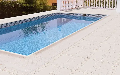 Piscina con borde de mosaico y suelos para piscinas que no quemen, de color claro y textura agradable.