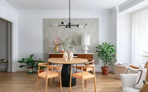 Comedor con mesa redonda de madera, sillas de cuero, lámpara moderna y plantas. Ideal para decorar piso moderno y elegante.