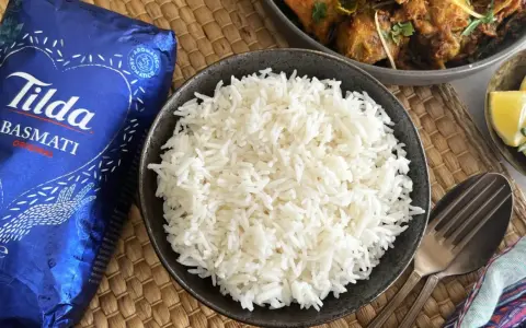 Un tazón de arroz basmati blanco y esponjoso junto a un paquete de Tilda Basmati Original.