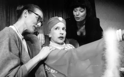 Marlena Milwiw młoda, w otoczeniu dwóch kobiet, w teatralnej scenie.