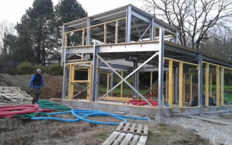 Chantier d'une maison ossature métallique. Le prix est un facteur clé pour ce type de construction moderne. Des tuyaux colorés sont visibles au sol.