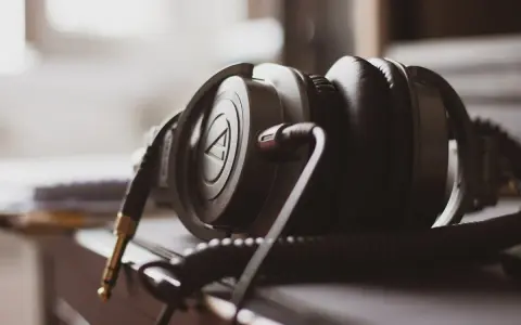 Gros plan sur un casque audio noir, avec son câble spiralé et sa prise jack dorée. La sensibilité du casque audio est palpable.