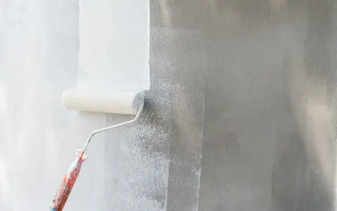 Rodillo blanco aplica pintura a pared gris. Se ve el proceso de cuantas manos de pintura se le da a una pared para un acabado perfecto.