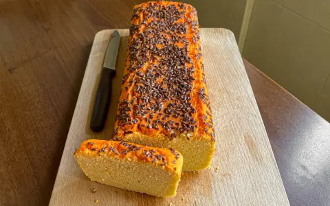 Pane di lenticchie con semi di lino, affettato su tagliere di legno, accanto a un coltello.