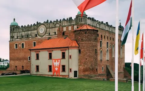 Majestatyczny zamek golubski z polską flagą i innymi flagami narodowymi na trawiastym dziedzińcu.