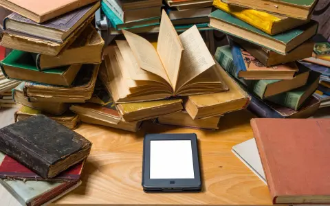 Stosy starych książek i nowoczesny ebook na drewnianym blacie. Wybór między tradycją a technologią.