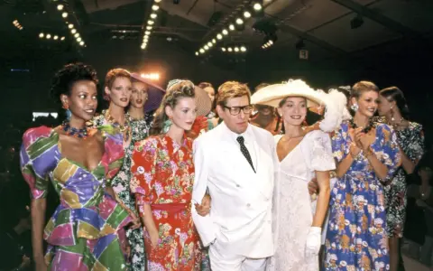 Models and designer Yves Saint Laurent at the Staley Wise Gallery fashion show, showcasing vibrant, patterned dresses and bold accessories.