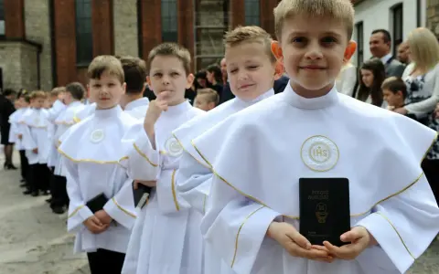 Chłopcy w białych albach, gotowi do komunii, trzymają modlitewniki. Jeden z nich uśmiecha się do aparatu.
