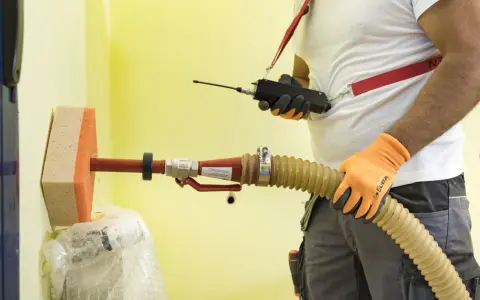 Un técnico usa un dispositivo para insuflar aire a través de una manguera y una esponja en una pared amarilla.