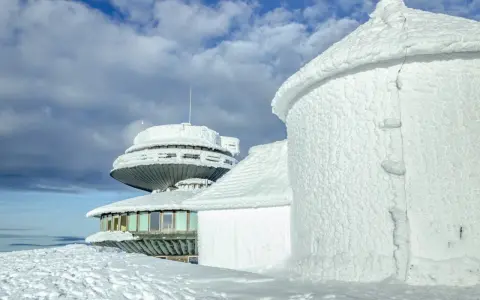 Zimowe krajobrazy na Śnieżce. Budynki obserwatorium pokryte lodem i śniegiem, niebo z chmurami.