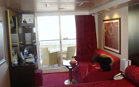 Cabina su MSC Divina, ponte 9, con balcone, divano rosso, letto e quadro astratto.