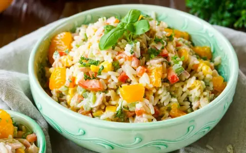 Erfrischender Reissalat mit Mandarinen, Paprika und Kräutern, garniert mit Basilikum.