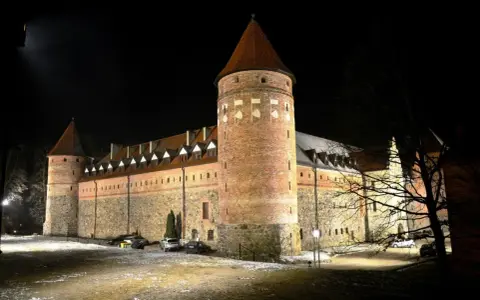 Zamek w Bytowie nocą, oświetlony, z wieżami i kamiennymi murami.