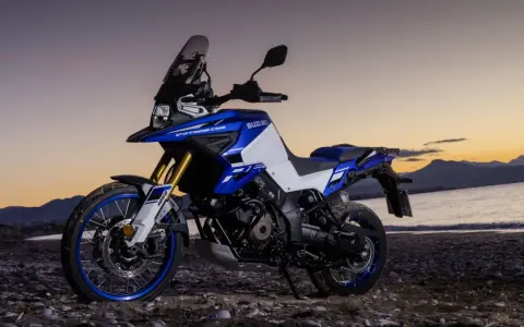 Suzuki V-Strom 1050 DE blu e bianca su una spiaggia al tramonto. Le opinioni su questa moto sono unanimi: avventura pura.