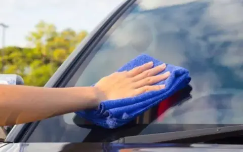 Mano con paño azul limpiando los cristales del coche para una visibilidad perfecta.