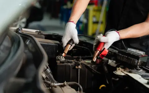 Manos enguantadas conectando cables a la batería del coche. Es hora de desconectar la batería del coche para un mantenimiento seguro.