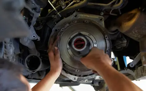 Mechanik dokonuje wymiany dwumasy w samochodzie, pracując przy skrzyni biegów.