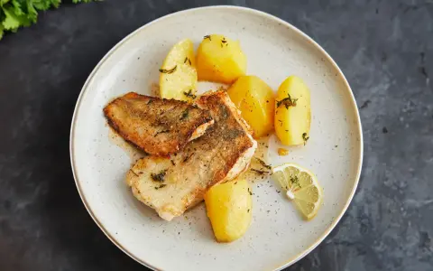 Gebratener Seehecht mit Haut, serviert mit Salzkartoffeln und Zitrone. Ein köstliches Gericht, das zeigt, wie man Seehecht mit Haut zubereitet.