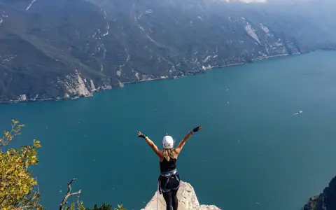Kobieta z rękami w górze na szczycie klifu, podziwiająca jezioro Garda po przejściu via ferrata.