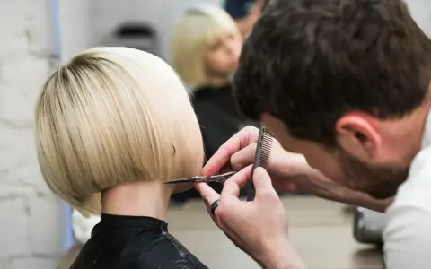 Fryzjerka tworzy modne fryzury odmładzające po 40 krótkie. Blond bob jest precyzyjnie cięty.