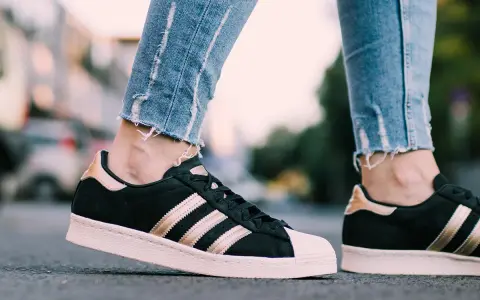 Nogawki jeansów i czarne **modele butów adidas z lat 2000.** ze złotymi paskami i różową podeszwą.